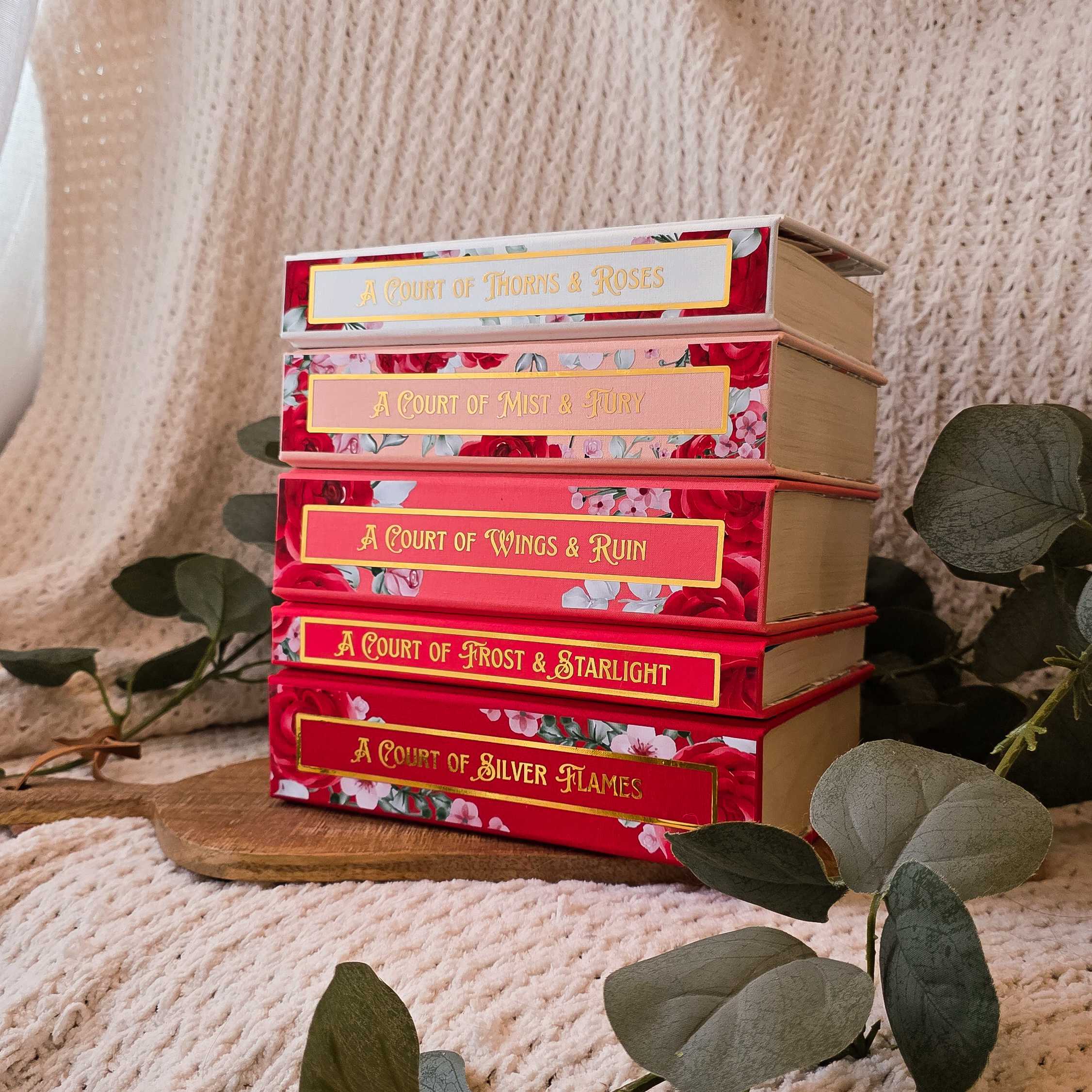 Stack of books titled 'A Court of Thorns & Roses' series on a wooden surface with a soft, textured background.