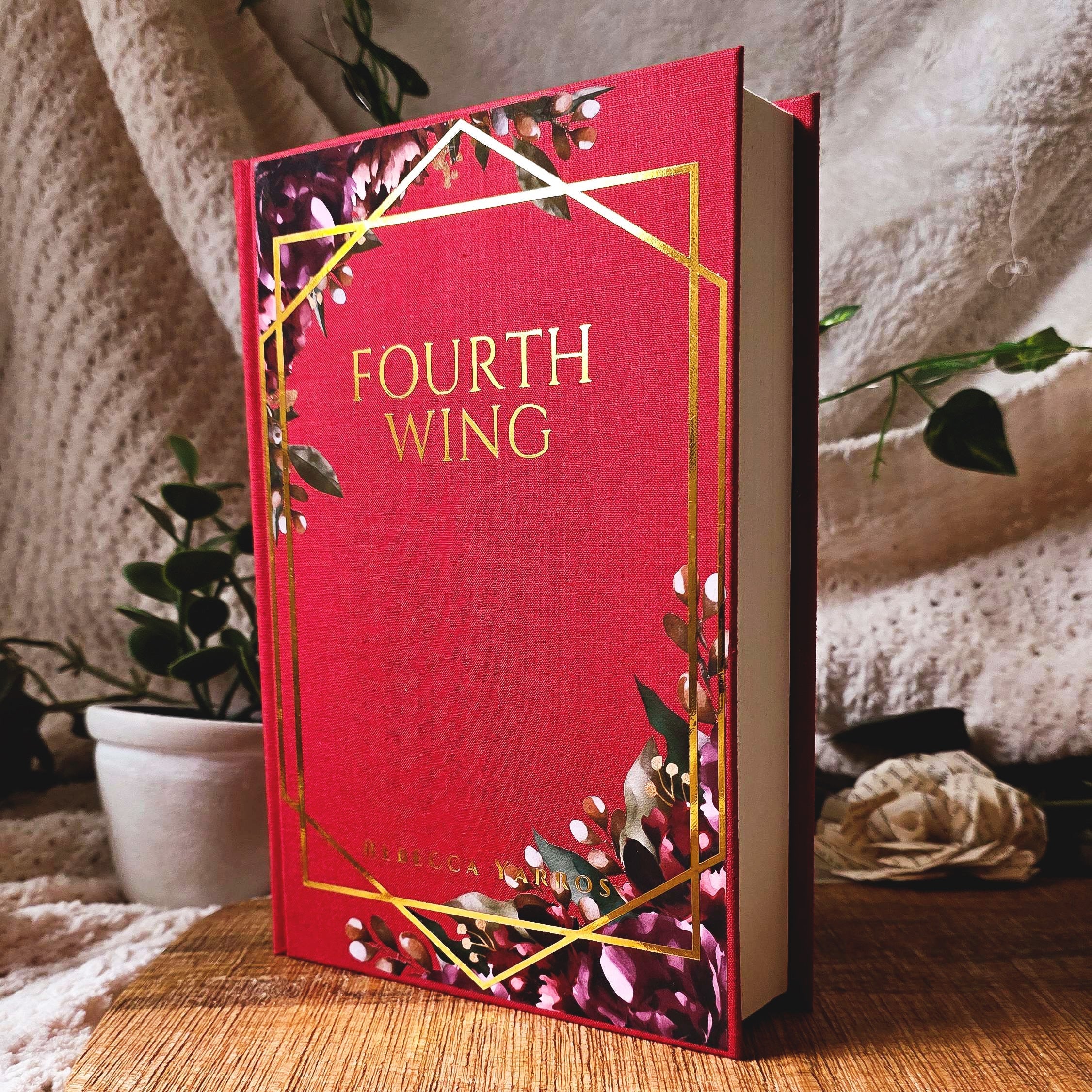 Red book titled 'Fourth Wing' on a wooden surface with a soft, neutral background