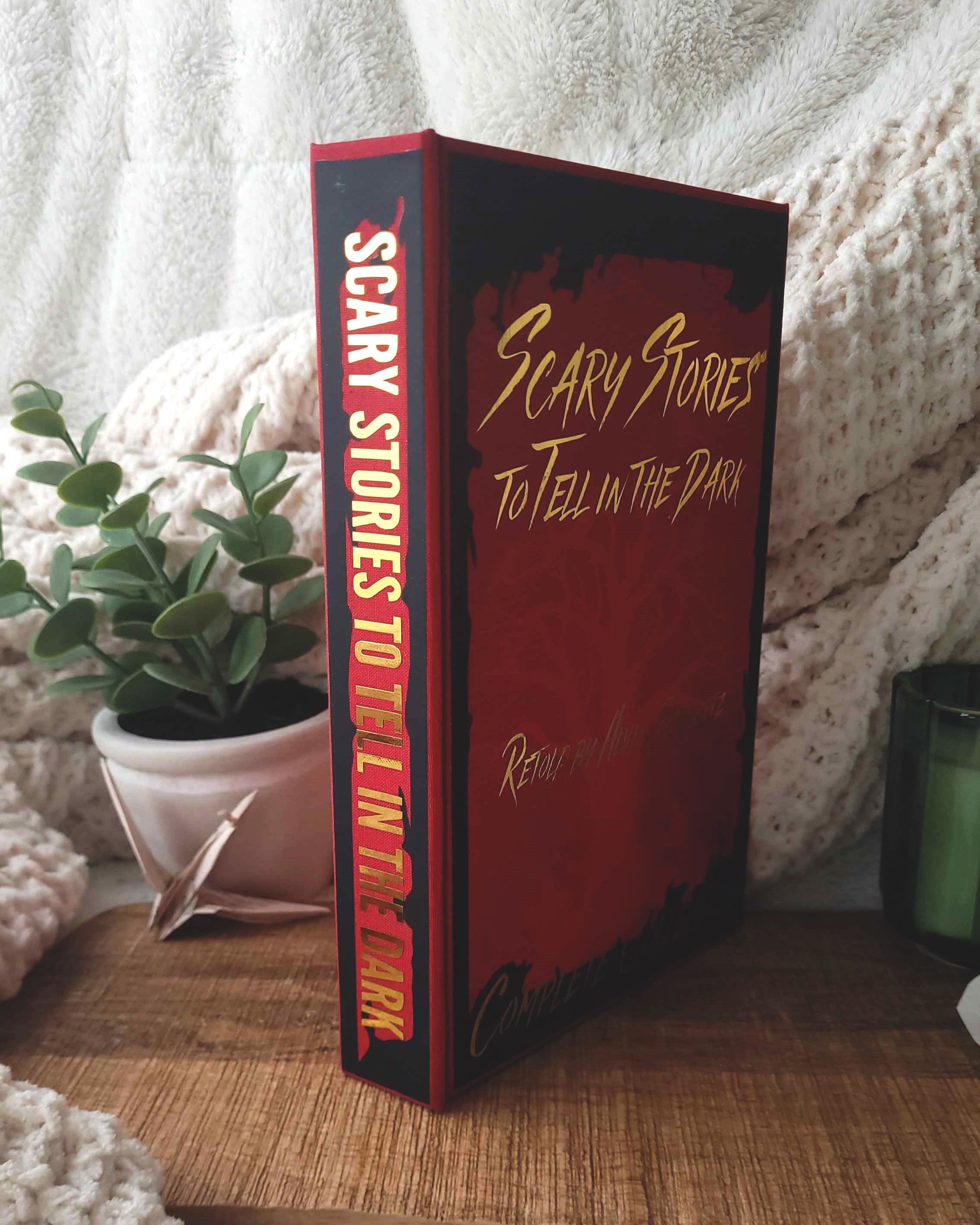 Book titled 'Scary Stories to Tell in the Dark' on a surface with a plant and candle in the background.
